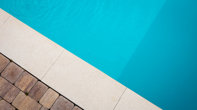 Abstract view of a swimming pool edge with turquoise water and stone pavers