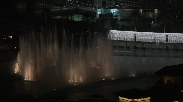 Dubai Fountain water jets rise in slow motion across Burj Lake beside illuminated Downtown Dubai buildings at night