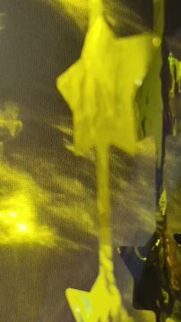 Close-up of translucent yellow star-shaped decorations hanging in a row, illuminated by warm golden light with dark star shapes and a softly blurred background.