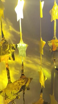 Close-up of translucent yellow star-shaped decorations hanging in a row, illuminated by warm golden light with dark star shapes and a softly blurred background.