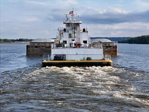 Towboat pushing covered barges along the wide Mississippi river under partly cloudy daylight conditions