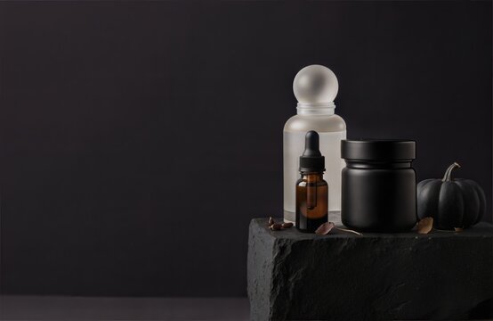 Luxury halloween skincare advertising. Amber dropper bottle, black jar and white bottle on dark stone podium with mini black pumpkin. Minimal premium cosmetic concept with copy space.