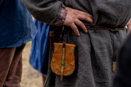 Medieval belt pouch made of brown leather with ornate brass plates worn on belt by reenactor in rustic linen tunic.