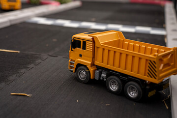 Yellow toy dump truck model parked on asphalt track during scale model exhibition or children play activity. © Marina