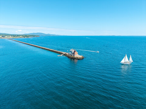 Aerial view of a two-masted schooner sailing past Rockland Breakwater Light and the long granite breakwater in Penobscot Bay near Rockland, Maine.