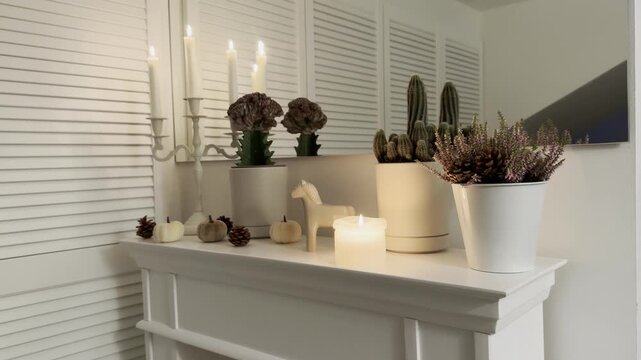 Horizontal 16:9 static shot of a white fireplace mantel decorated in a cozy hygge and modern classic style in 4K 60fps. Features a horse, potted heather, cactus, small decorative pumpkins, pinecones, 
