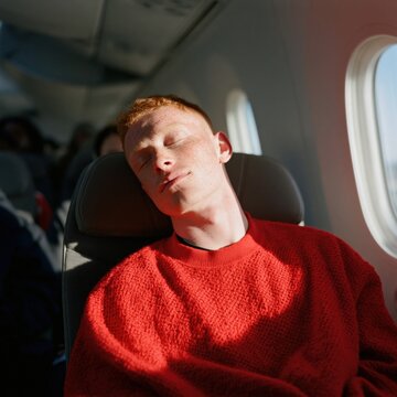 Man dozing with eyes closed on airplane seat near window in morning light for travel background and relaxation banner