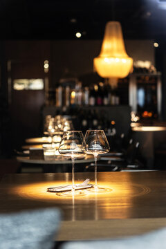 Two empty wine glasses on wooden table in atmospheric dimness of restaurant with chandelier in background. Elegant restaurant ambiance created