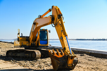 A bright yellow excavator located at a construction site on the riverbank. © SGr