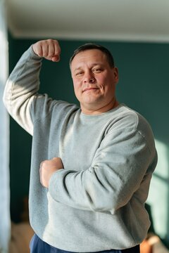 Man flexing arm in a casual sweatshirt in an indoor portrait showing confidence and strength for wellness and lifestyle content