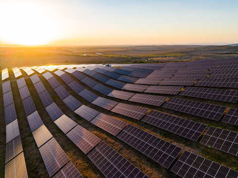 Solar panels capture sunlight on a farm in the late afternoon near a valley with a sunset in the background