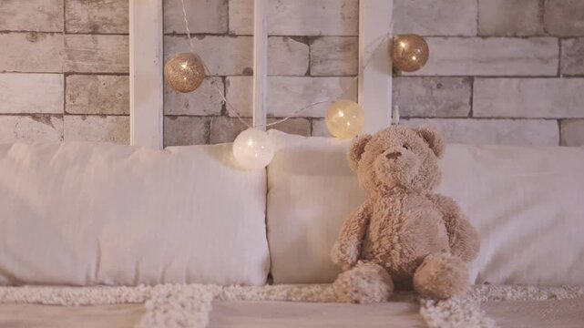 Bed with unlit decorative fairy lights in bedroom, teddy bear resting, soft beige blanket with white pillows, glowing string fairy lights in background, cozy calm home atmosphere, Evening relaxation