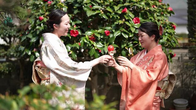 A woman in a patterned kimono holds a wooden kendama with a red ball as a woman in an orange kimono watches. Japan, April 19, 2025, spring.