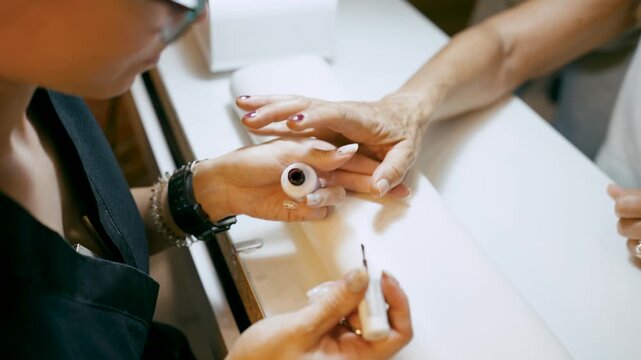 Skilled beautician carefully applying a coat of dark red nail polish to a client's fingernails during a professional manicure service