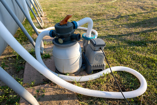 Swimming pool sand filter and pump system connected by hoses and electrical wiring, maintaining water clarity for summer relaxation and outdoor activity in a garden