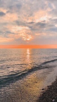 Calm waves at sunset. Wave splashing over pebbles at sea with foam. Rolling ocean waves. Summer paradise beach background at sunset