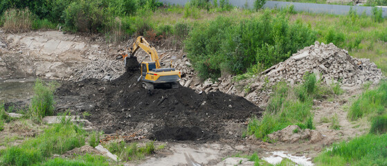 Yellow hydraulic crawler excavator digger working with soil at construction site, heavy machinery moving dark ground during earthmoving works near debris pile, industrial development background.  © Dmitry Presnyakov
