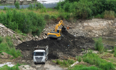 Yellow excavator loading soil into dumper truck bed at construction site, heavy machinery and tipper lorry moving dark ground during earthmoving works, industrial development logistics background.  © Dmitry Presnyakov