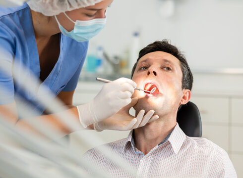 Man is sitting in armchair during dental diagnosis at dentist appointment. Girl doctor conducts examination procedure, identifies problem areas and tests sensitivity of teeth