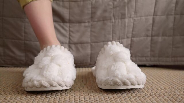 Woman putting on cozy fluffy slippers at home. Person getting out of bed in the morning, putting on a pair of comfortable and soft white fluffy slippers before walking away