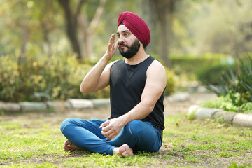 Fototapeta premium Concept of young sikh man yoga at park.. Cheerful sardar in lotus pose sitting on green grass. Concept of calm and meditation.. young man practicing yoga in park. 