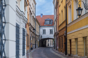 Fototapeta premium Narrow cobblestone street with historic colorful buildings and an archway in Warsaw, Poland.