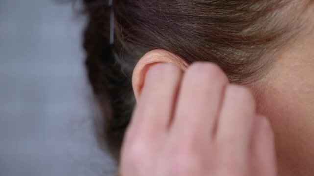 Woman inserting custom silicone earplugs for noise protection. Close-up view of a woman's hands carefully inserting custom-molded silicone earplugs into her ear canal for hearing protection