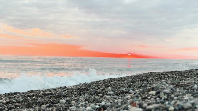 Calm waves at sunset. Wave splashing over pebbles at sea with foam. Rolling ocean waves. Summer paradise beach background at sunset