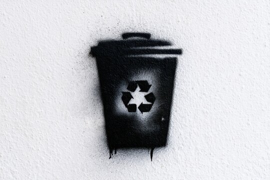 Black spray paint stencil of a recycling bin with recycling symbol on a white textured wall promoting environmental awareness and waste management