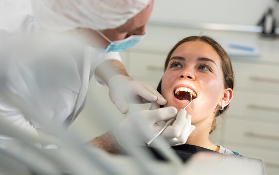 Girl is sitting in armchair during dental diagnosis at dentist appointment. Senior man doctor conducts examination procedure, identifies problem areas and tests sensitivity of teeth