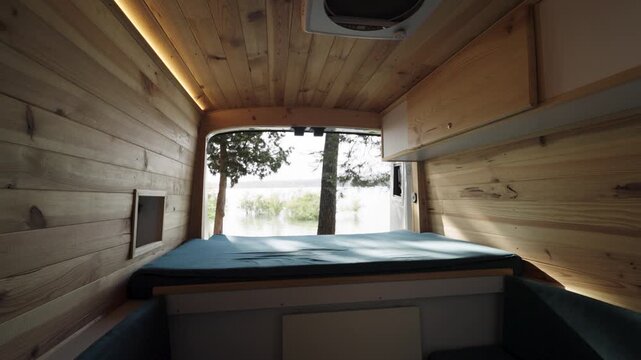 Interior of a custom built camper van with wooden paneling and a bed overlooking a serene lake, perfect for a digital nomad lifestyle