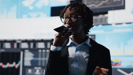 Businesswoman shares a voice note with a coworker by smartphone while reviewing performance metrics...
