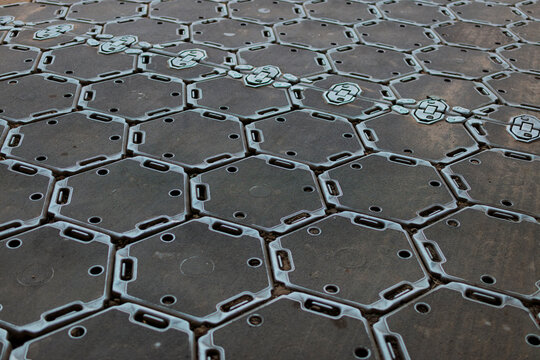 Close view of interlocking plastic trackway panels forming a hard standing over soft sand, a repeating hexagonal pattern.