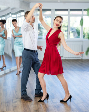 Interested young adult couple in formal wear, bride and groom, rehearsing elegant wedding waltz in studio under guidance of professional female choreographer in bright studio