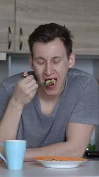 Exhausted and sleepy young man eating a healthy breakfast of cereal and oatmeal in his kitchen, starting his day with a nutritious meal as part of his daily routine and healthy lifestyle