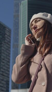 Elegant businesswoman talking on the smartphone on a sunny day in a modern city district with skyscrapers, expressing a range of positive and serious emotions