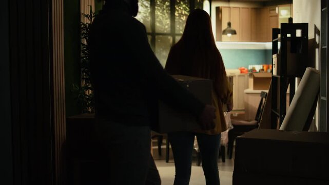 Young homeowners carry boxes through their new house on moving day, celebrating the achievement of buying a first home while unpacking belongings and beginning a proud new chapter together.