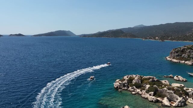Aerial view of a high-speed Jet Ski creating a powerful wake in deep blue Mediterranean water near a rugged rocky coastline. (Kayalık bir kıyının yakınında, derin mavi Akdeniz suyunda g&uuml;&ccedil;l&uuml; bir su izi