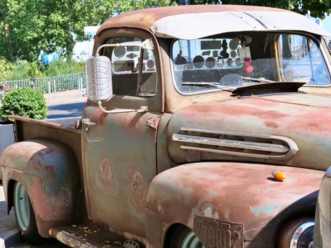 Rustic rusty vintage pickup truck with weathered green patina finish and retro chrome mirror parked outdoors on a sunny summer day.