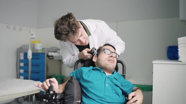 Young male doctor conducting a medical examination of a man with spina bifida sitting in a wheelchair inside a hospital room