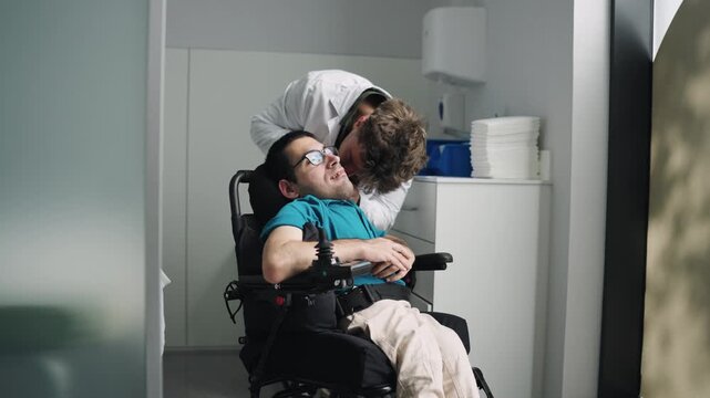 Young male patient with spina bifida sitting in a wheelchair during a medical examination. A doctor is checking his physical condition