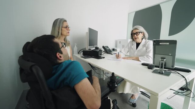 Senior doctor explaining diagnosis to a young patient with spina bifida in a modern wheelchair, accompanied by his attentive mother