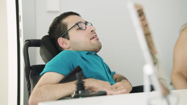 Young man with spina bifida sitting in an electric wheelchair. He is smiling while having a conversation in a bright hospital room