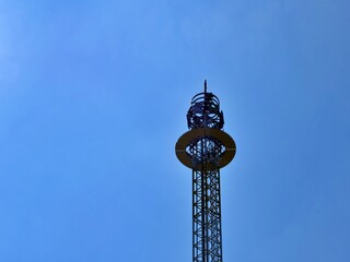 Tall free fall tower attraction silhouetted against a vibrant solid blue sky at an amusement park or fairground site. © Ena
