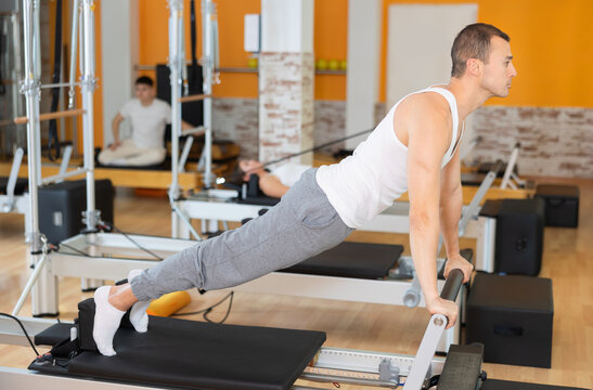 Man with help of informer is engaged in Pilates studio and performs exercises to strengthen muscles of press. Round-robin training for athletes during preparation for competitions
