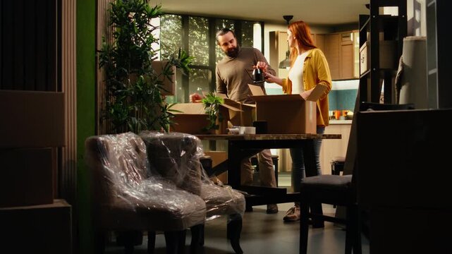 Happy couple unpacks wrapped belongings inside a new house, enjoying relocation, first home ownership and the satisfaction of arranging decorations indoors.