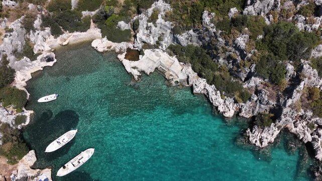 Aerial top-down video of small white boats anchored in a hidden rocky cove with crystal clear turquoise water in Kekova, Turkey.