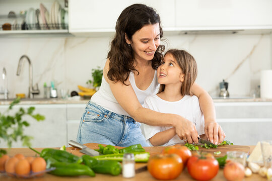 Mom helps her daughter chop parsley to decorate salad. Woman assist child during cooking, helps to hold knife correctly