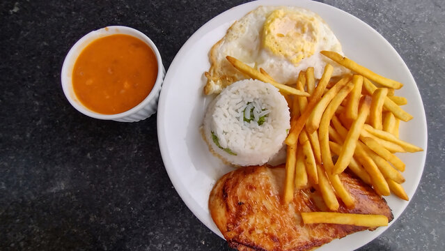 Traditional Brazilian lunch meal called prato feito with grilled chicken fillet, white rice, french fries, fried egg, and brown beans