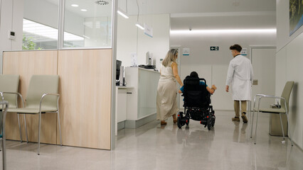 Fototapeta premium Woman pushing a person in a wheelchair with a doctor walking beside them in a modern hospital corridor, showing healthcare and support